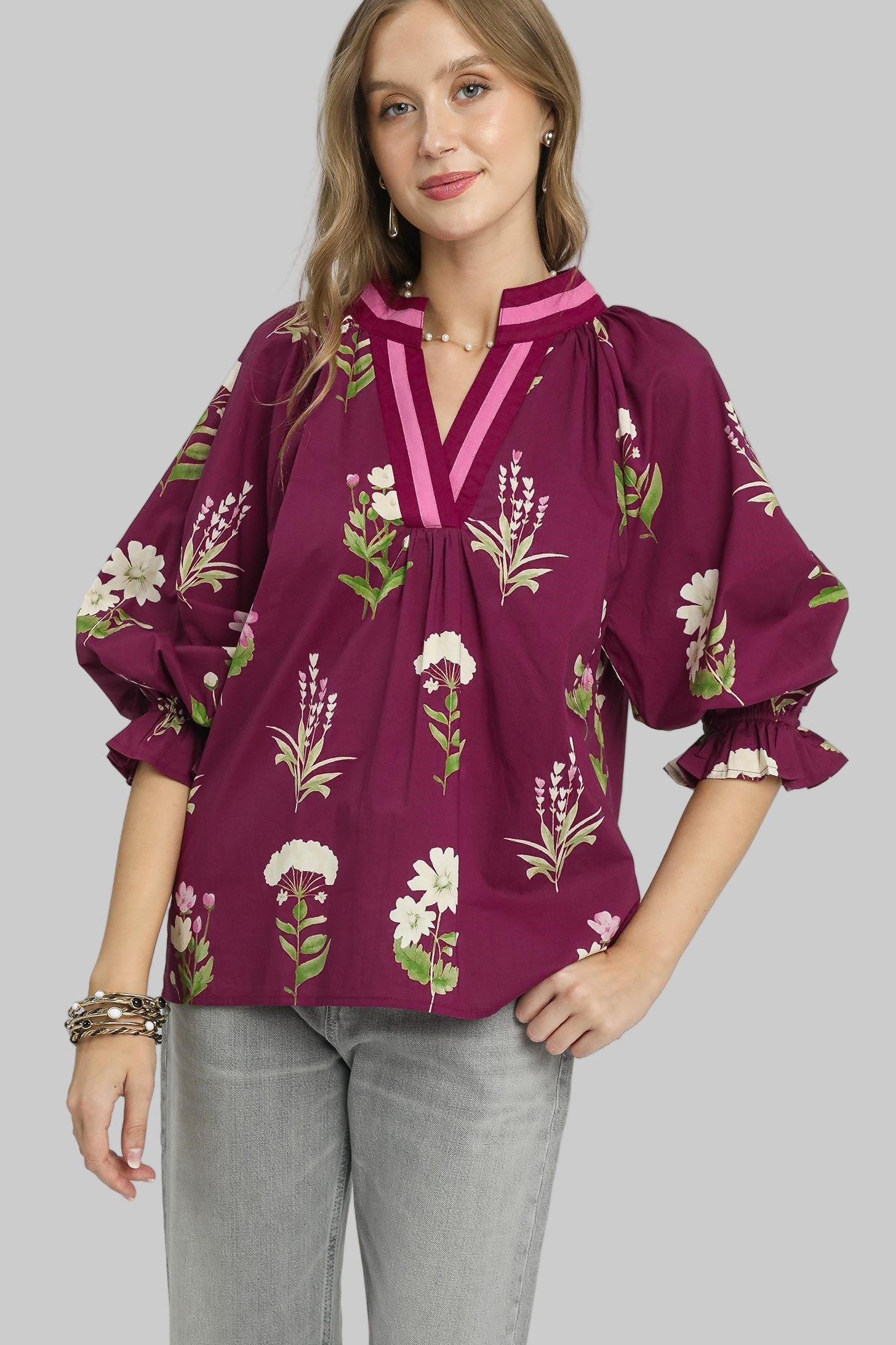 Woman wearing a plum-colored blouse with floral patterns on a gray background
